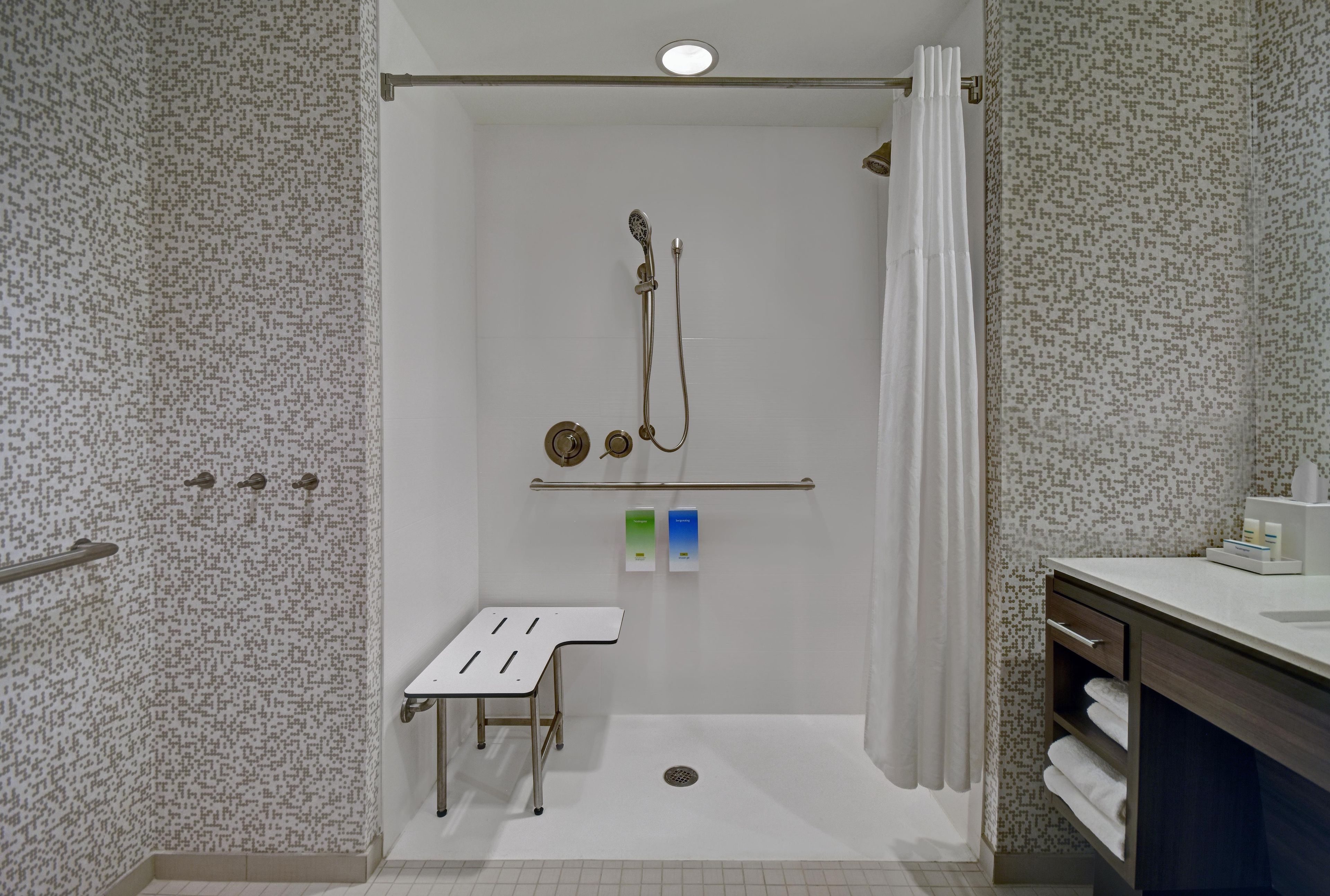A shower with a handheld showerhead, a small stool, and a towel rack.