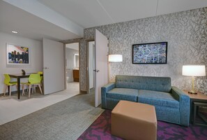 A hotel room with a sofa, a dining table with chairs, a small table with a lamp, and a large framed map on the wall. - Home2 Suites by Hilton Atlanta Airport North (Atlanta)
