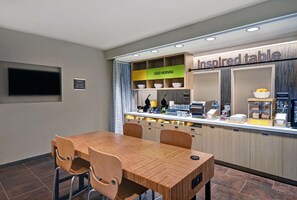 Un espace cuisine moderne avec une table et des chaises en bois, un comptoir où sont disposés divers aliments, et une pancarte sur laquelle on peut lire : « Table d’inspiration ».