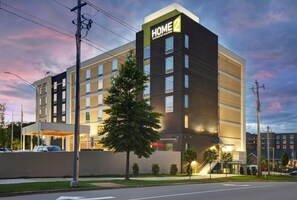 Un hotel de varios pisos con un llamativo letrero 'HOME 2', una entrada cubierta y un estacionamiento.