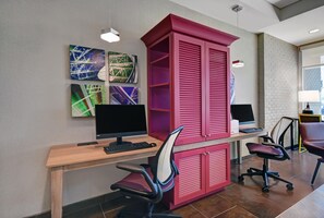 Un espacio de oficina moderno con un escritorio de madera, dos monitores negros, un archivador rojo y una silla de oficina negra.