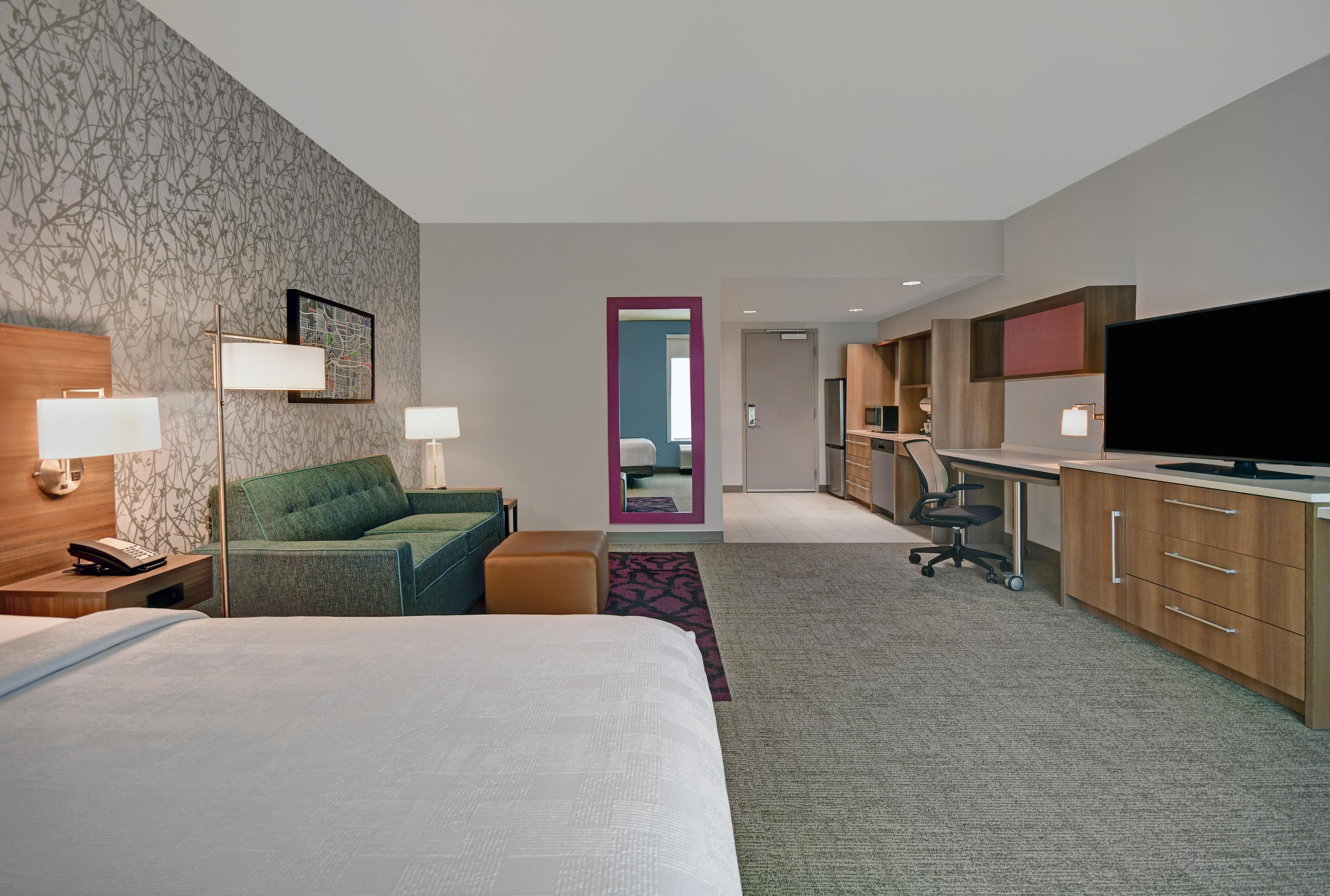Une chambre d’hôtel comprenant un lit, un canapé, un bureau avec un ordinateur, une télévision et un miroir.