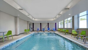 A swimming pool with a tiled edge, surrounded by green chairs and tables, with a staircase in the background. - Home2 Suites by Hilton Atlanta Airport North (Atlanta)