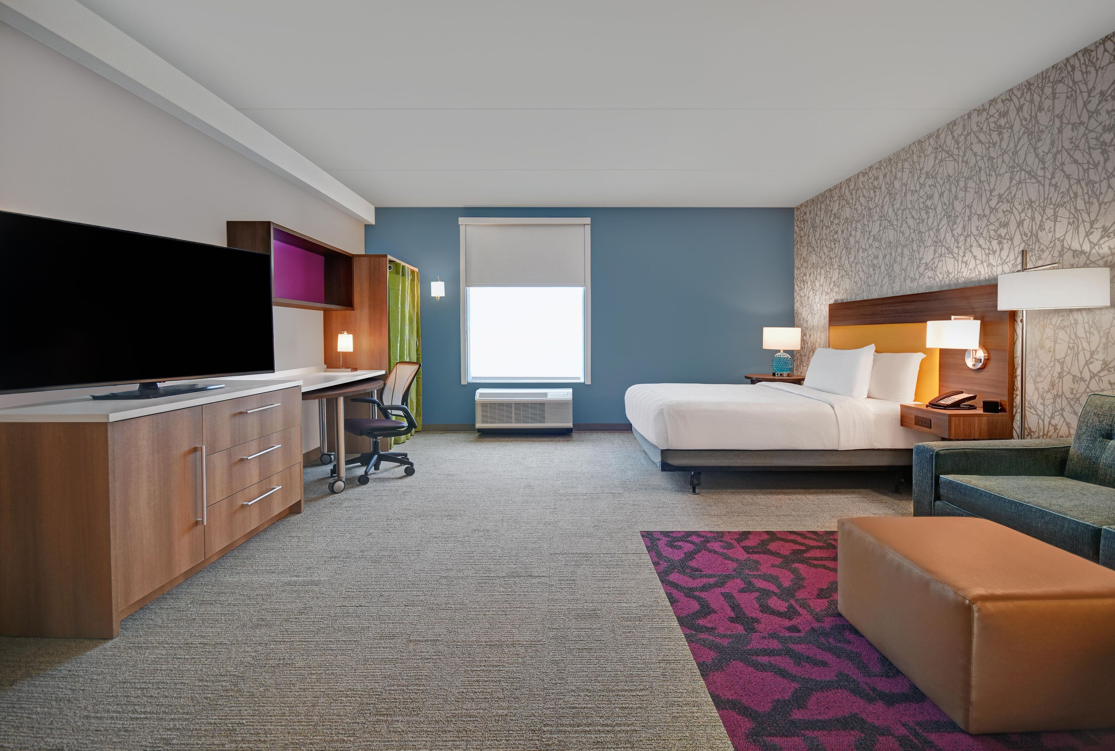 Habitación de hotel con cama, escritorio, televisor y vistas al exterior.