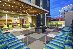 Un espace extérieur aménagé en patio, avec des sièges, un foyer et des guirlandes lumineuses.