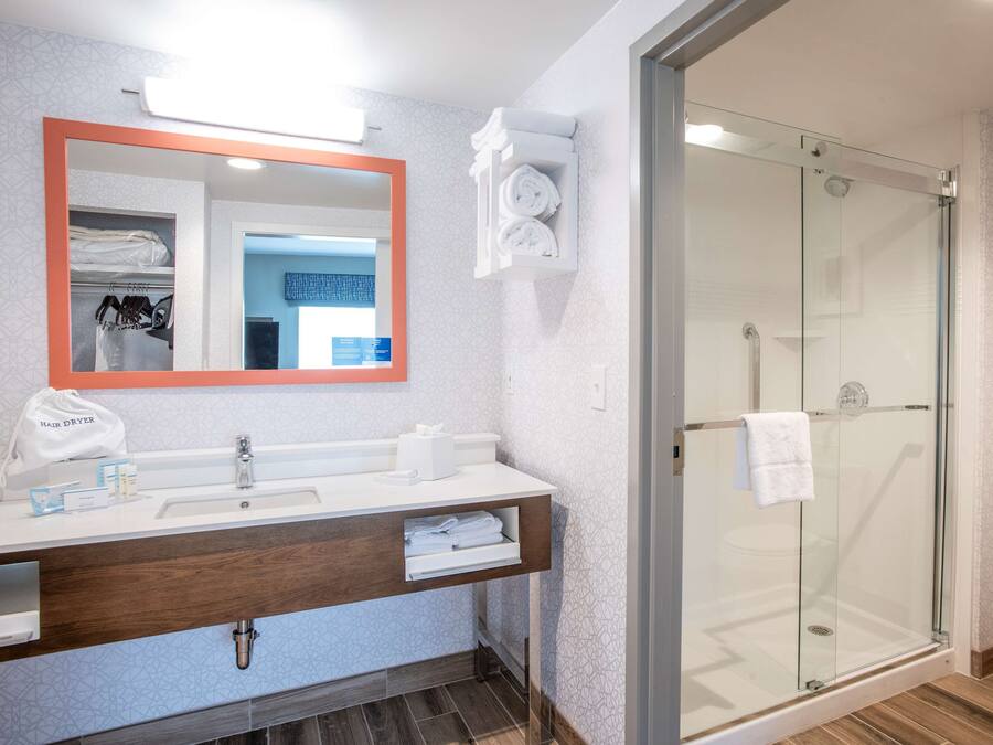 Un baño moderno con ducha de vidrio, un espejo grande y un tocador con toallero.