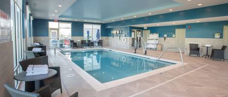 A swimming pool area with lounge chairs and a table, a reception desk, and a view of the outside.