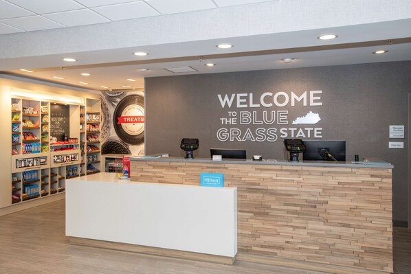 Un espace d’accueil avec une pancarte indiquant « BIENVENUE DANS L’ÉTAT DU BLUE GRASS » et un comptoir portant l’inscription « Hilton ».