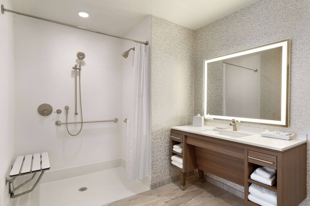 Une salle de bain moderne dotée d’une douche à l’italienne, d’un grand miroir et d’un meuble-lavabo avec un évier et un porte-serviettes.