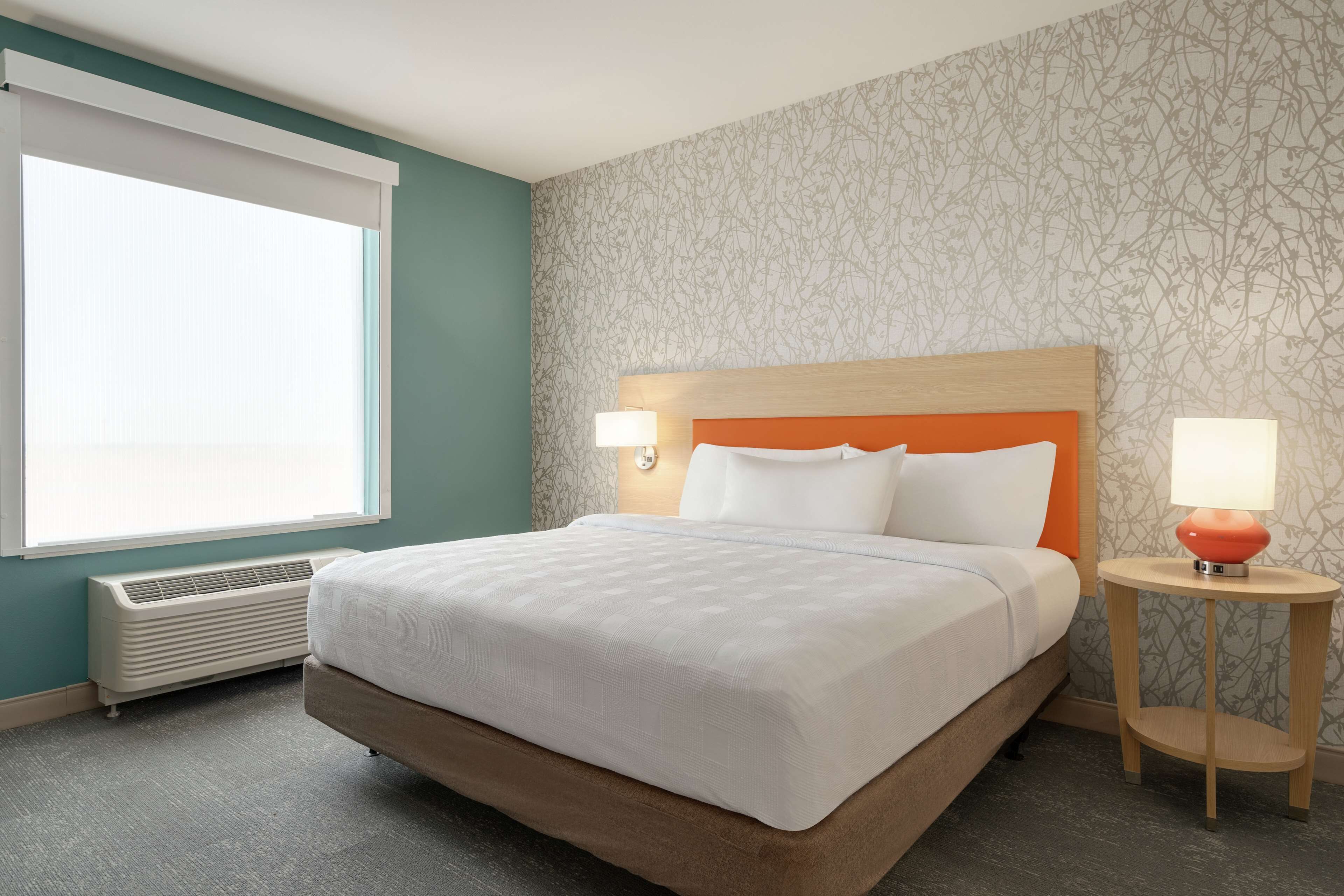 A hotel room with a large bed, two bedside lamps, a heater, and a window with blinds.