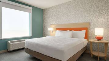 A hotel room with a large bed, two bedside lamps, a heater, and a window with blinds.