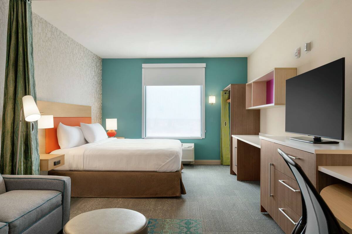 Une chambre d’hôtel avec un lit, un bureau, une chaise, une télévision et une fenêtre.