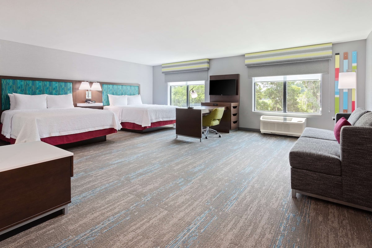 A hotel room with two beds, a desk, a chair, a TV, and a couch.