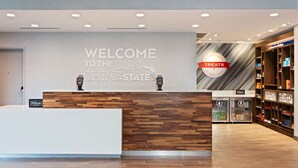 A reception desk with a "Welcome to the Sun Shine State" sign, a "Treats" sign, and a minibar area with a "Hilton" sign. - Hampton Inn & Suites Alachua I-75 (Alachua)