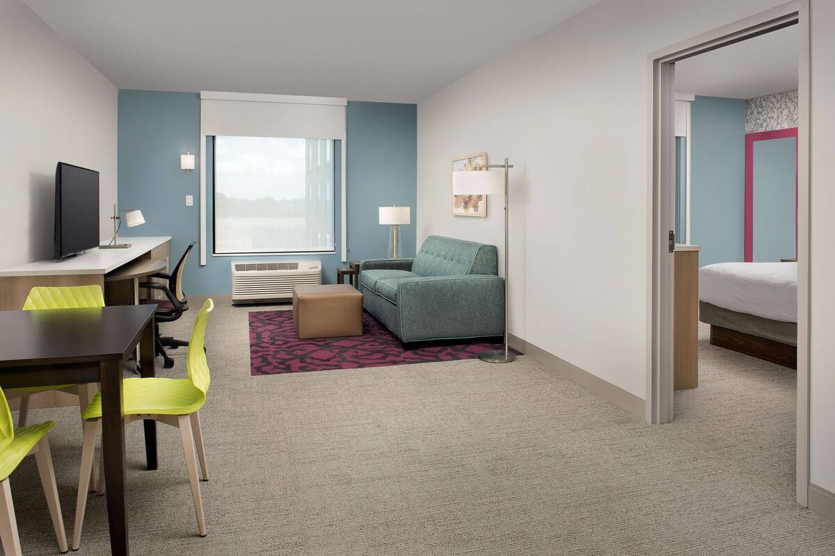 Une chambre d’hôtel avec un bureau, un canapé vert, un lit et une fenêtre donnant sur un beau paysage.