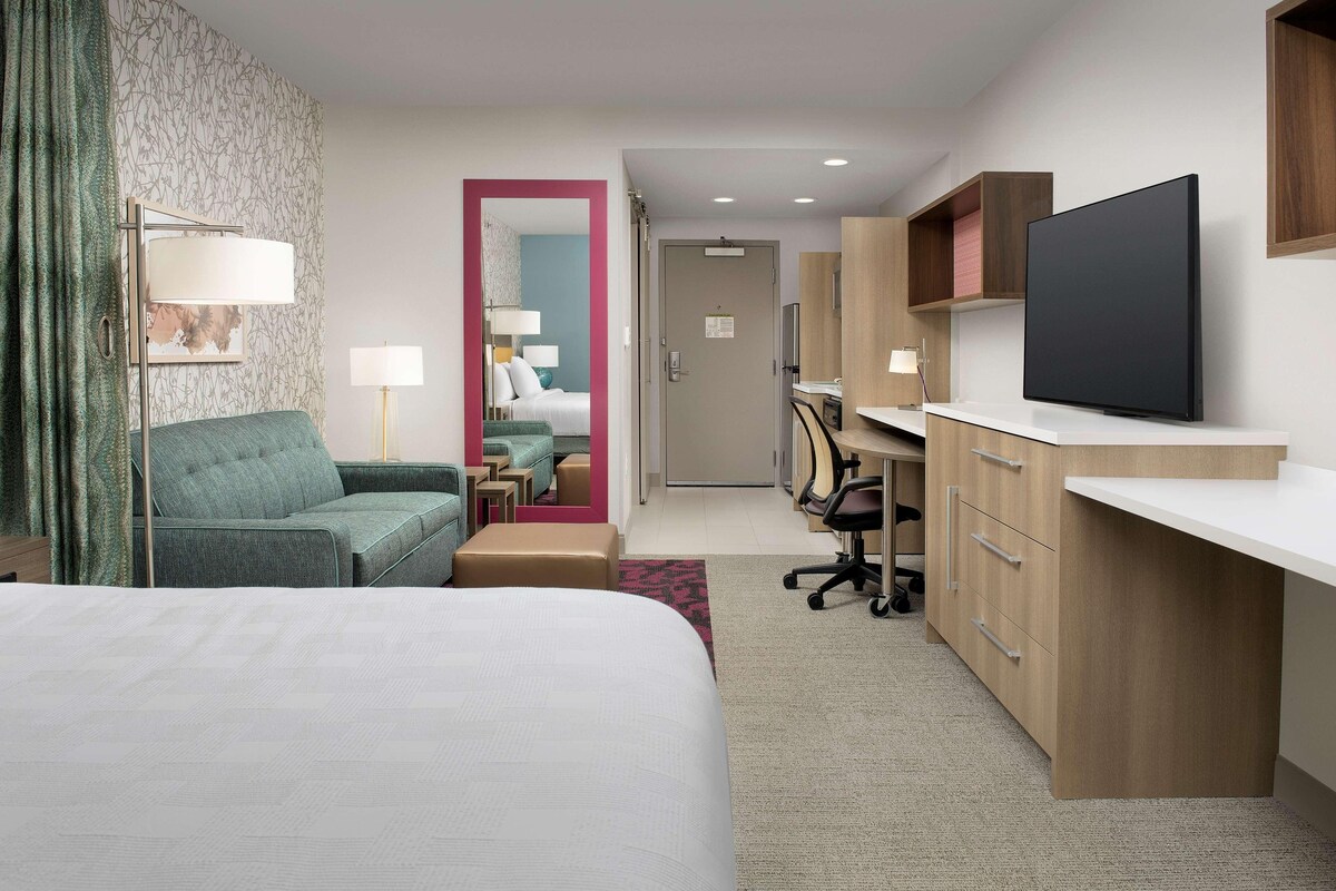 A hotel room with a bed, a desk, a television, a chair, and a mirror.