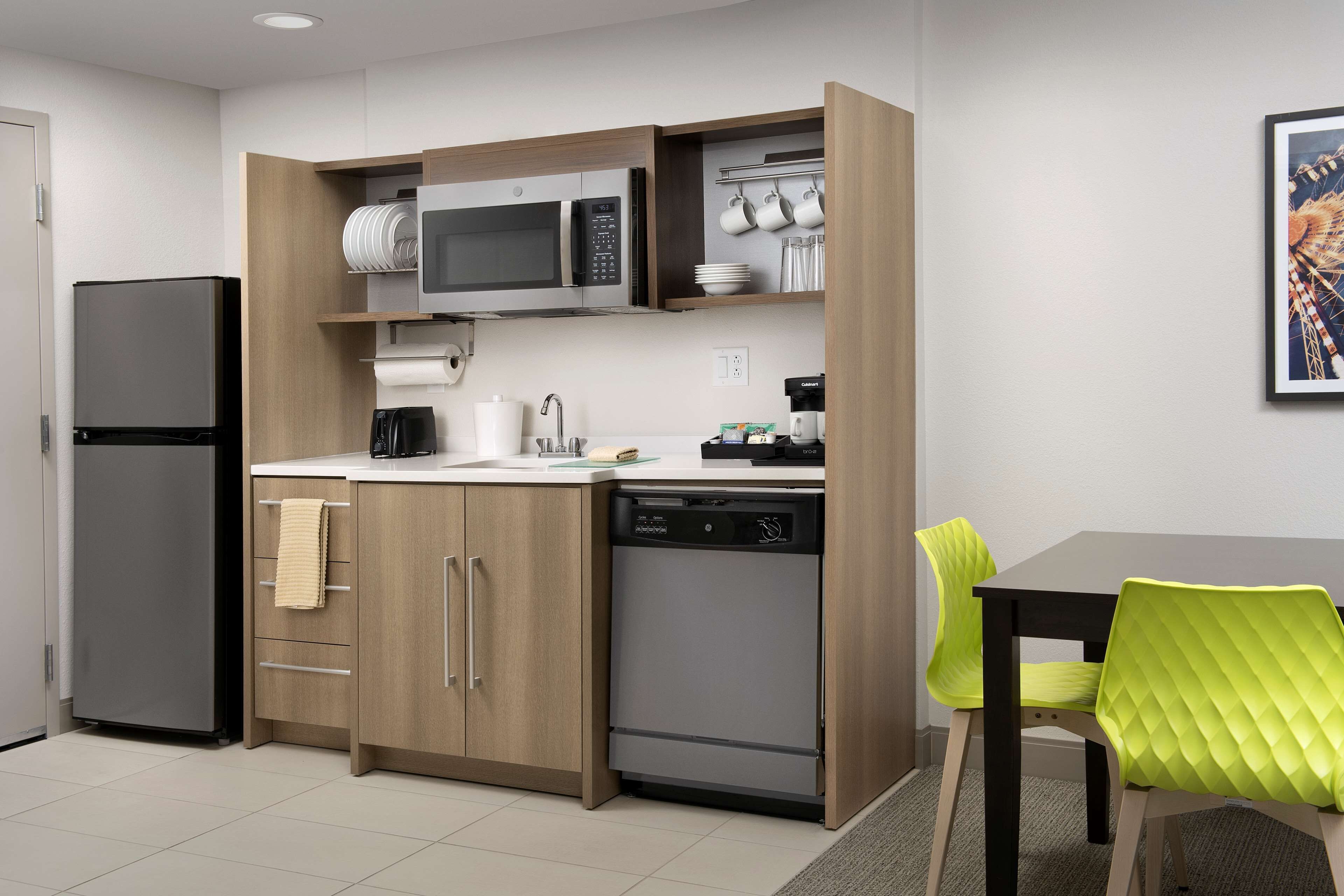 A compact kitchen with a microwave, coffee maker, and dishwasher. There is a dining table with two chairs.
