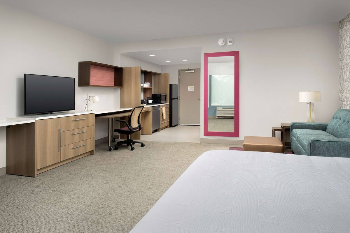 Une chambre d’hôtel comprenant un lit, un bureau avec un ordinateur, une télévision, une kitchenette et une salle de bain.
