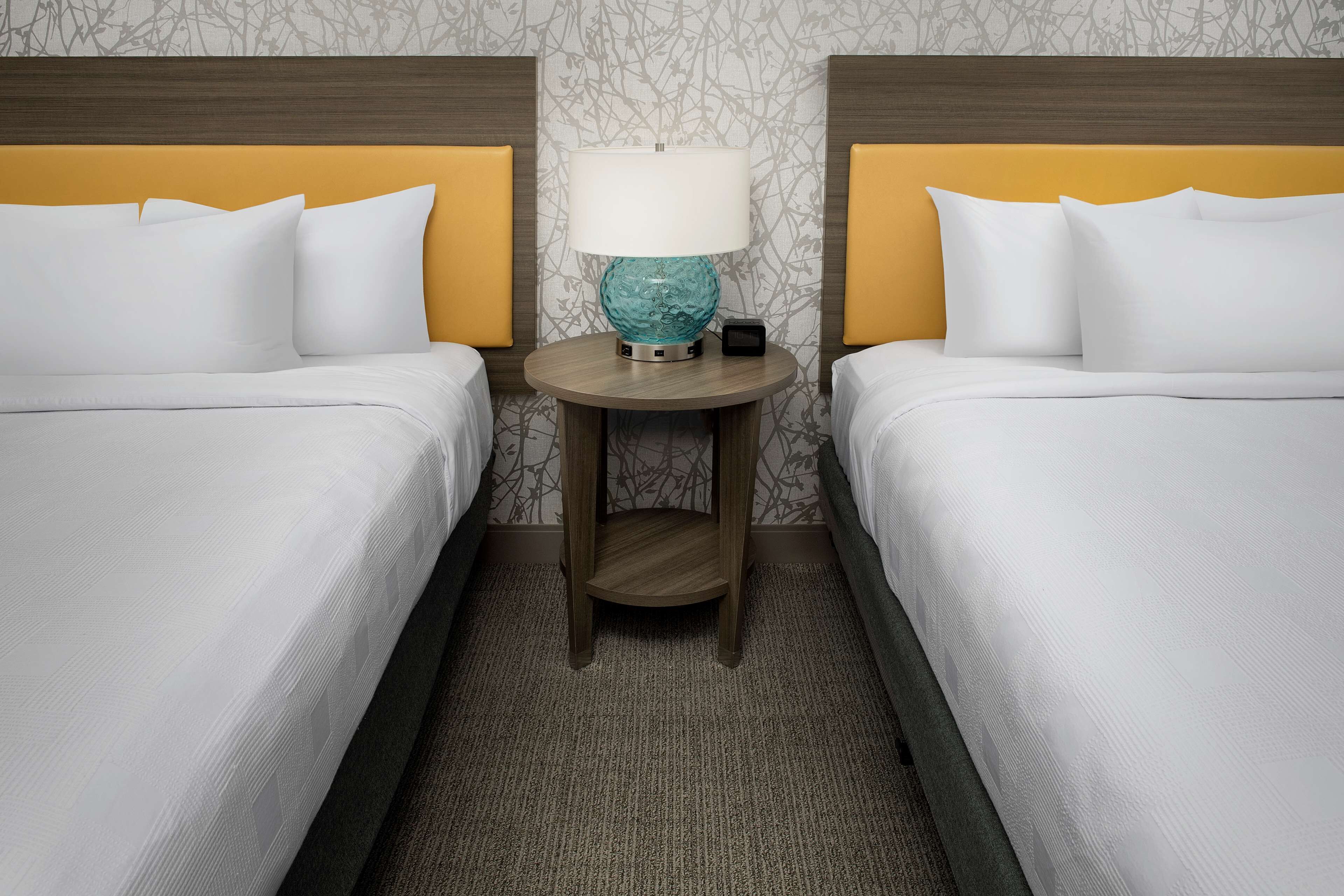 A hotel room with two beds, a round table with a lamp, and a patterned wallpaper.