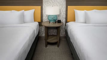 A hotel room with two beds, a round table with a lamp, and a patterned wallpaper.