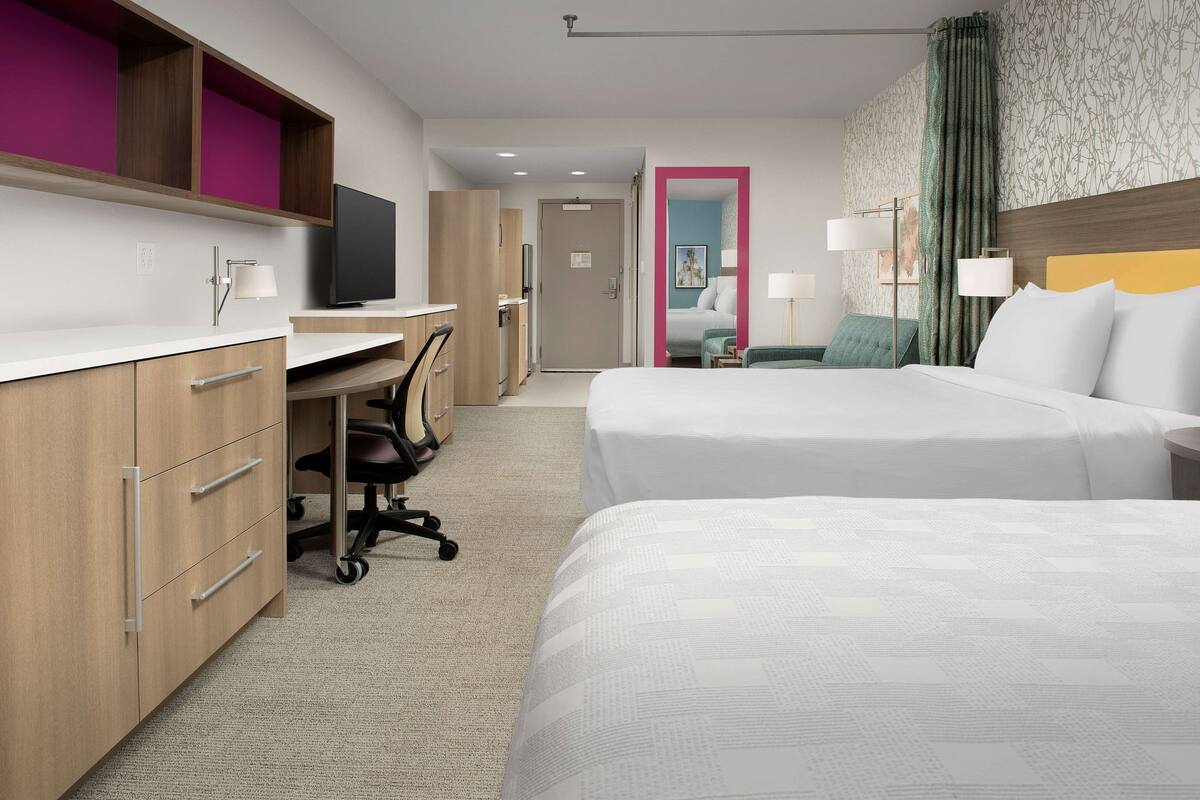 Une chambre d’hôtel avec deux lits, un bureau, une chaise et un téléviseur.