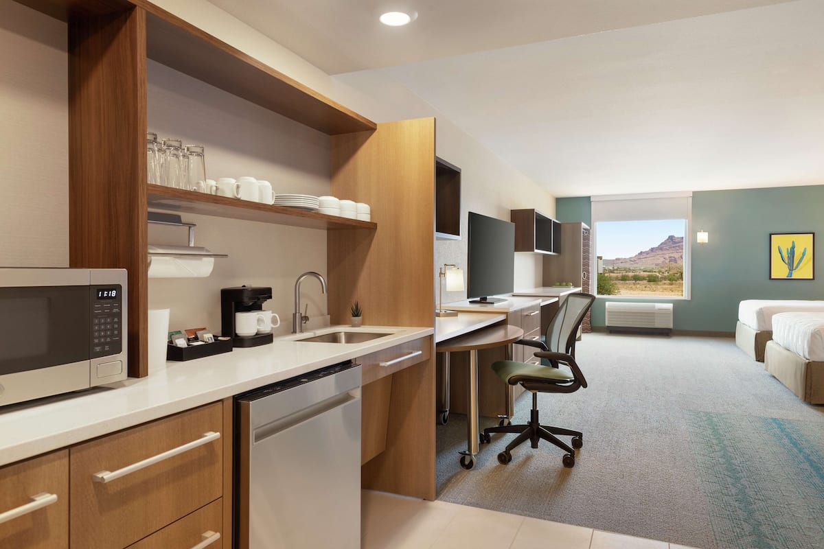 A modern hotel room with a kitchenette, a desk, a bed, and a view of the desert landscape.