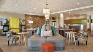 A modern lobby with a seating area, a kitchen, and a reception desk. - Home2 Suites by Hilton Mesa Longbow, AZ (Mesa)