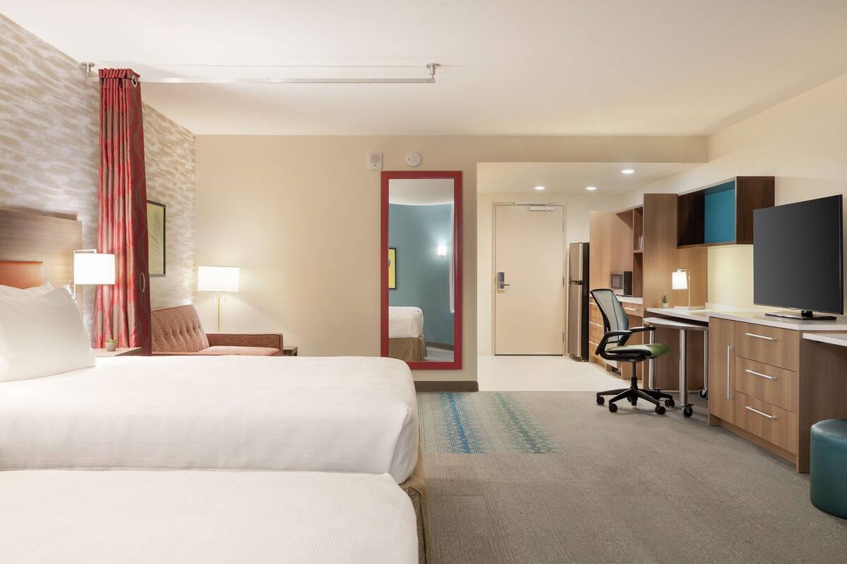 A hotel room with two beds, a desk, a television, and a mirror.