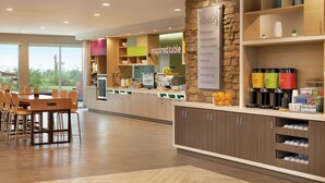 A modern kitchen area with a dining table and chairs, a stone accent wall, and various kitchen appliances and storage cabinets. - Home2 Suites by Hilton Mesa Longbow, AZ (Mesa)