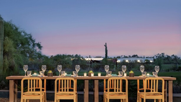 An outdoor dining table set with chairs, string lights, and a sunset view. - Home2 Suites by Hilton Mesa Longbow, AZ (Mesa)
