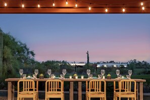 An outdoor dining table set with chairs, string lights, and a sunset view. - Home2 Suites by Hilton Mesa Longbow, AZ (Mesa)