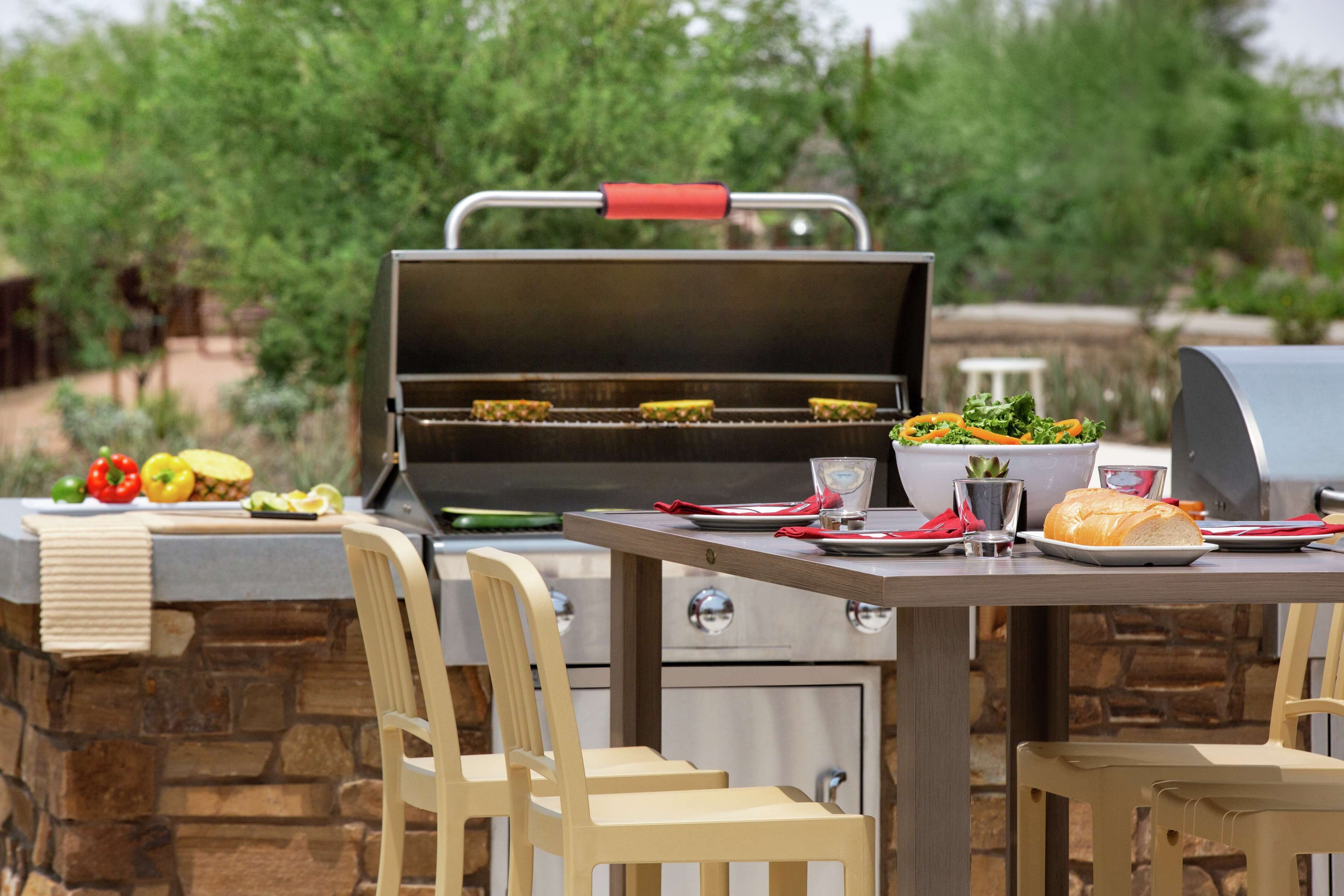 An outdoor dining area with a grill, stone walls, and wooden chairs.