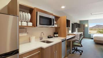 A modern kitchen with a microwave, sink, and cabinets. There is a desk with a chair and a bed with a mountain view.