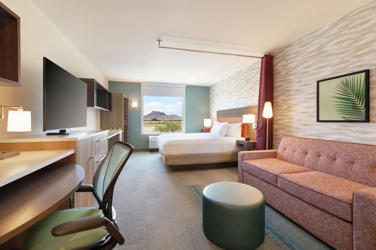 A hotel room with a bed, a desk with a computer, a chair, a sofa, and a TV.