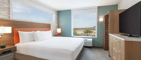 Habitación de hotel con una cama grande, televisor, escritorio con lámpara y vista al desierto.