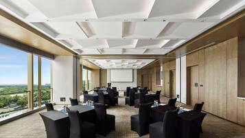 A conference room with multiple tables and chairs, large windows offering a view of the city, and a projector screen on the wall.