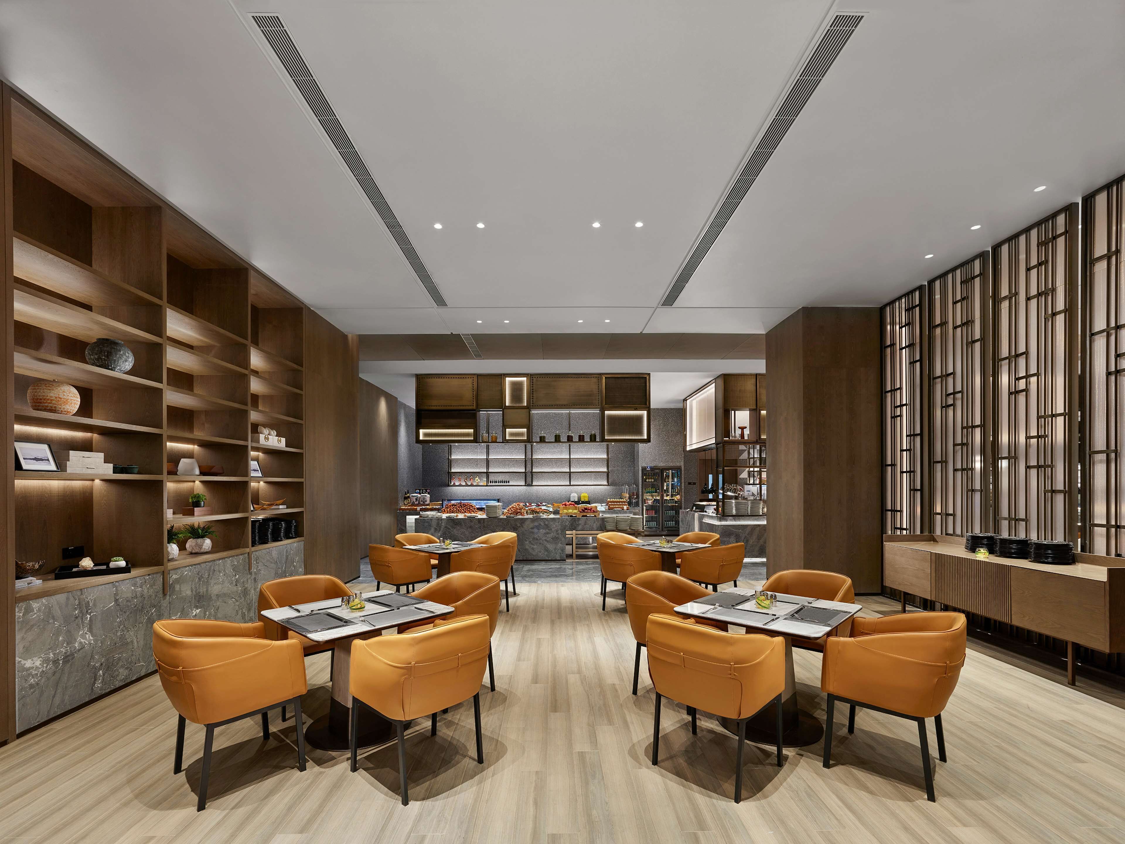 A modern dining area with wooden paneling, marble countertops, and orange chairs.