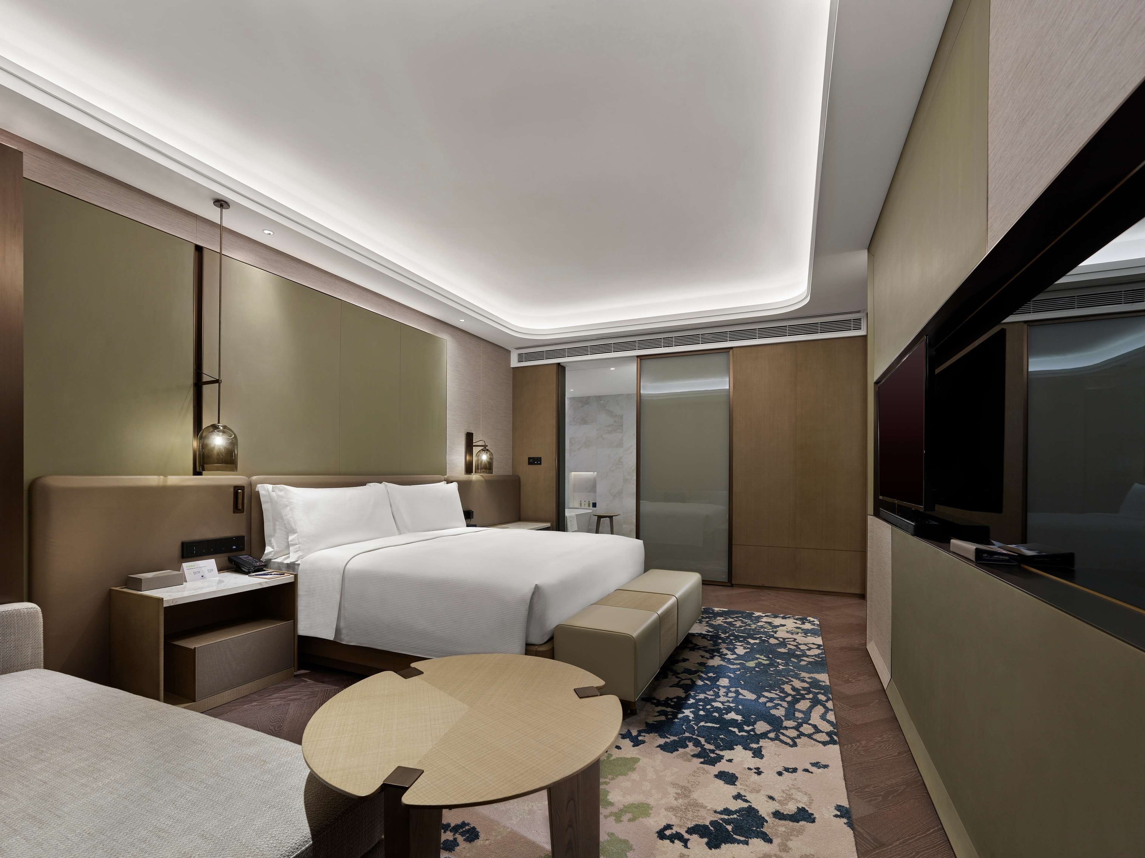 Una habitación de hotel moderna con una cama grande, mesitas de noche, un televisor y un pequeño rincón de descanso.