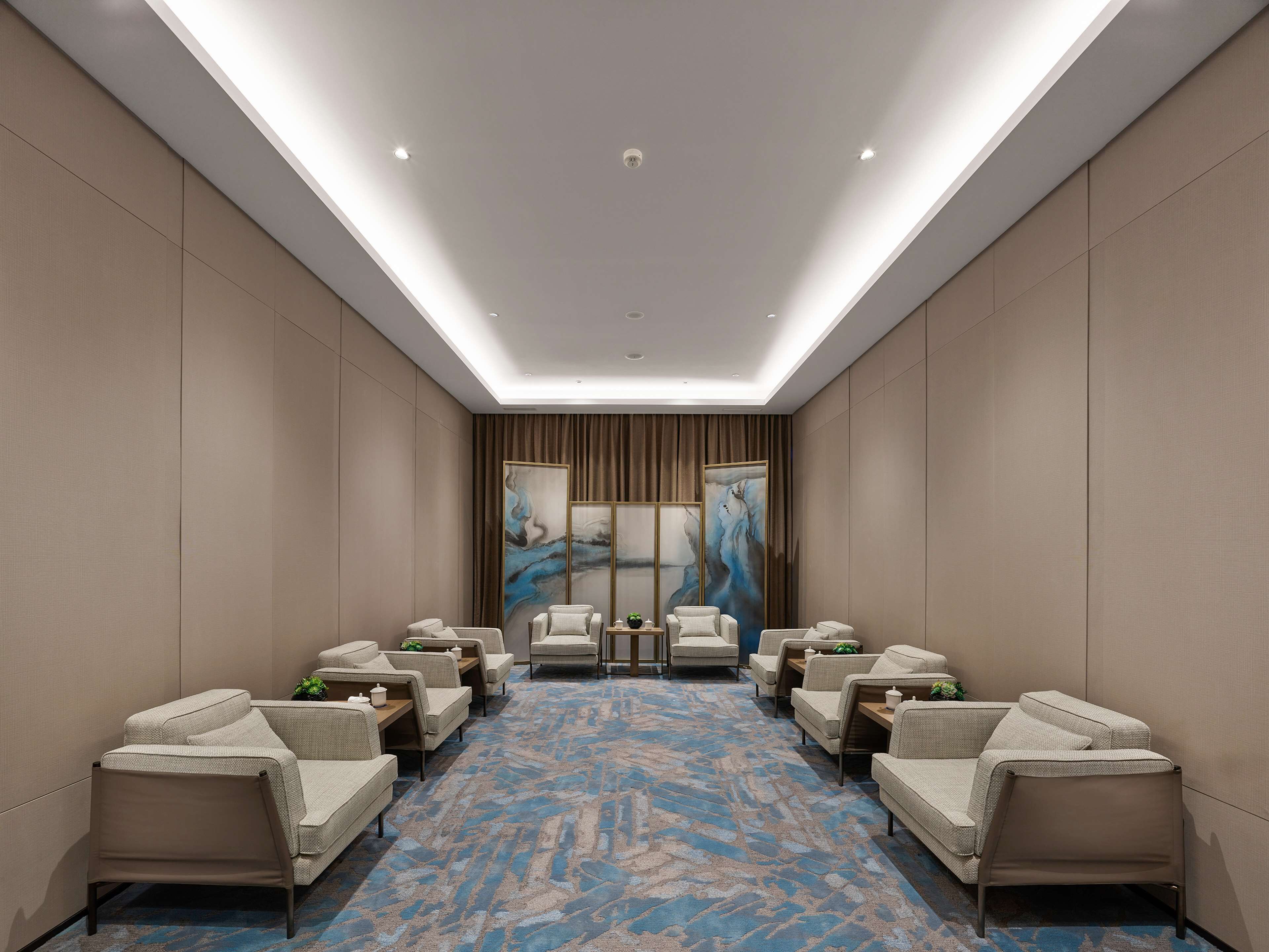 A conference room with a blue patterned carpet, beige walls, and a ceiling with recessed lighting.