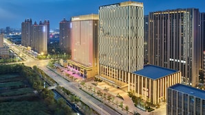 A modern hotel with a prominent vertical facade, multiple high-rise buildings in the background, and a well-lit urban street scene. - DoubleTree by Hilton Qidong, China (Nantong)