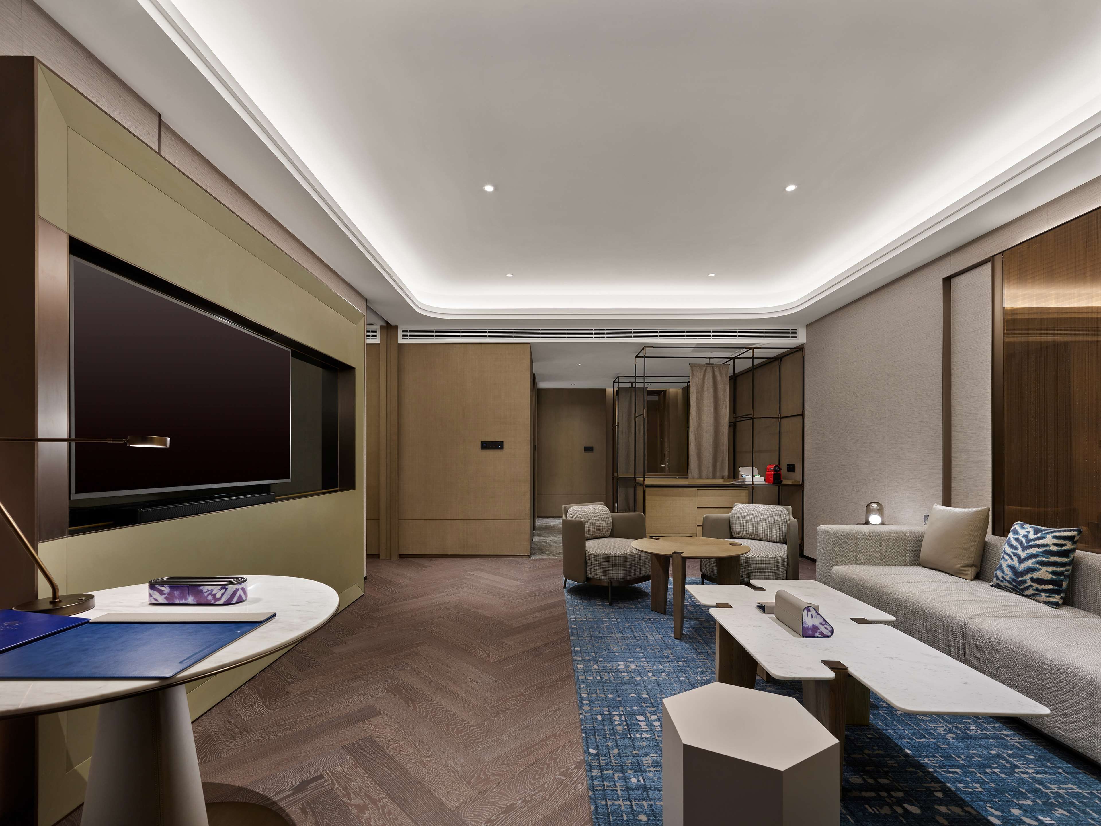 A modern hotel room with a flat-screen TV, a sofa, a coffee table, and a small dining table.