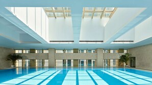 A large indoor swimming pool with clear blue water, surrounded by large windows and concrete walls. - DoubleTree by Hilton Qidong, China (Nantong)