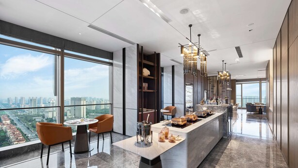 A modern kitchen with a marble countertop, a dining area with chairs, and a view of the cityscape through large windows. - DoubleTree by Hilton Qidong, China (Nantong)