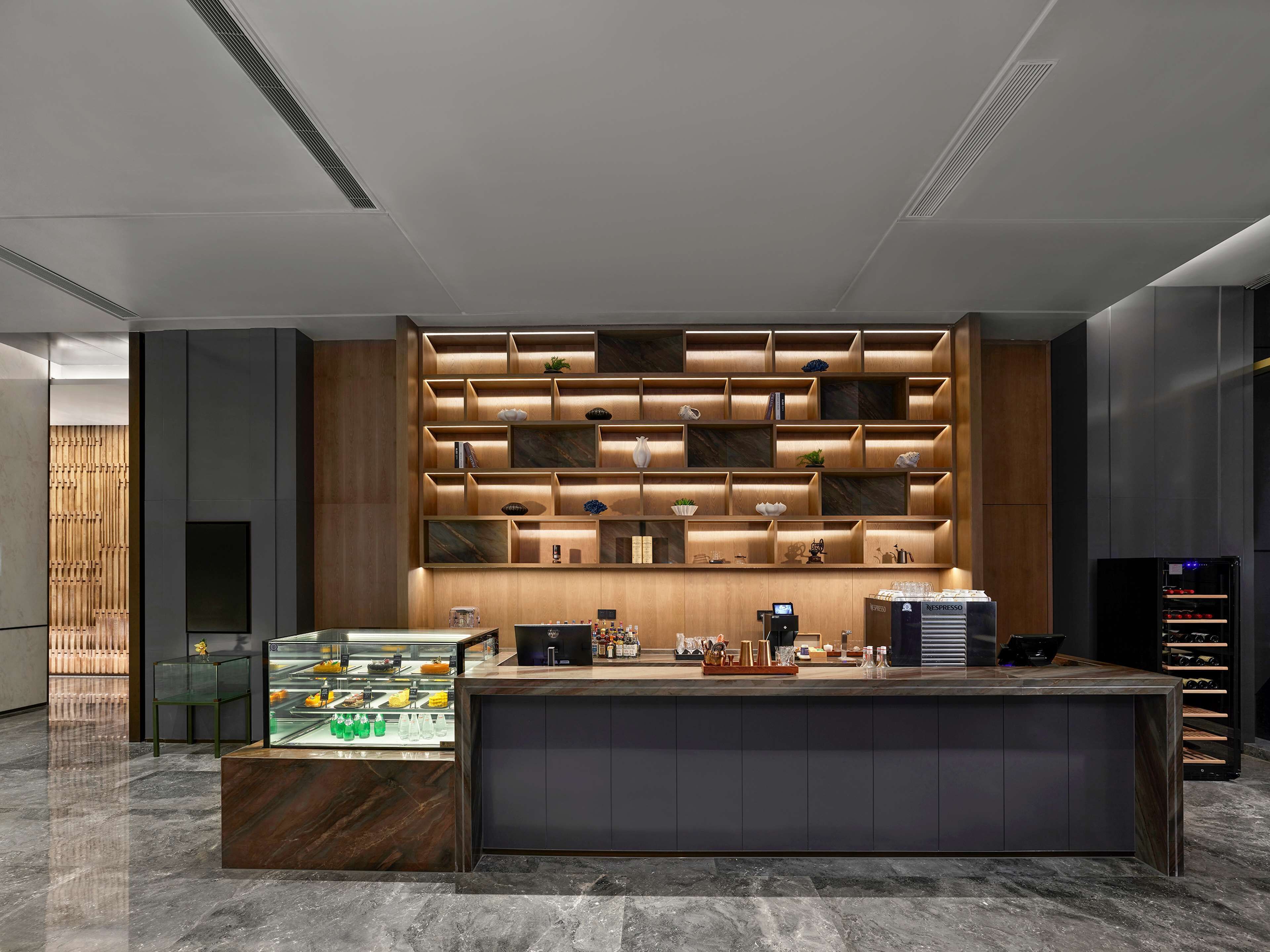 Una moderna zona de recepción con mostrador de mármol, estanterías de madera con varios objetos y una cafetera.