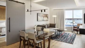 A modern living room with a sofa, a dining table with chairs, a large window with a view, and a sliding door.