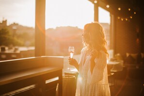 A person holding a glass of wine in an outdoor setting with a view of the sunset.