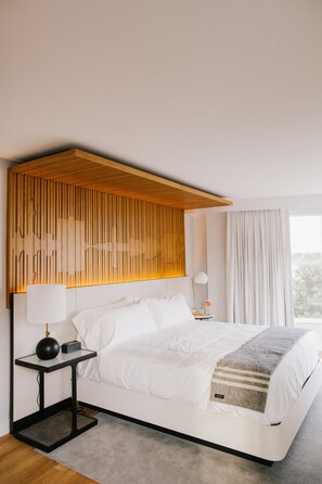 A modern hotel room with a large bed, a wooden headboard, a bedside table with a lamp, and a view of the outdoors through a window. - Canopy by Hilton Portland Waterfront (Portland)