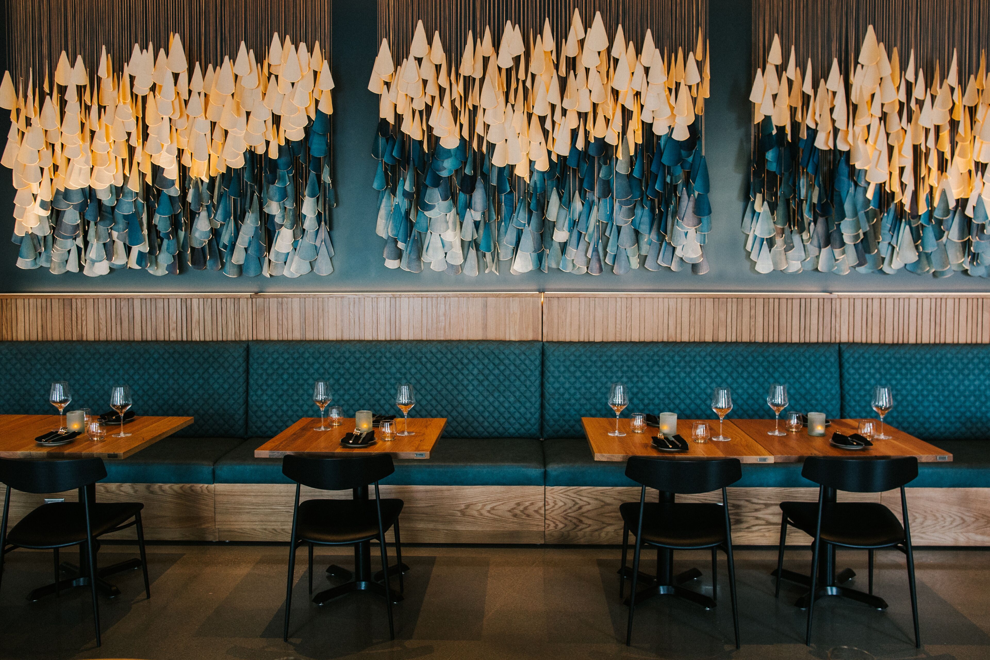 A restaurant interior with wooden tables, black chairs, and a wall decorated with hanging light fixtures.