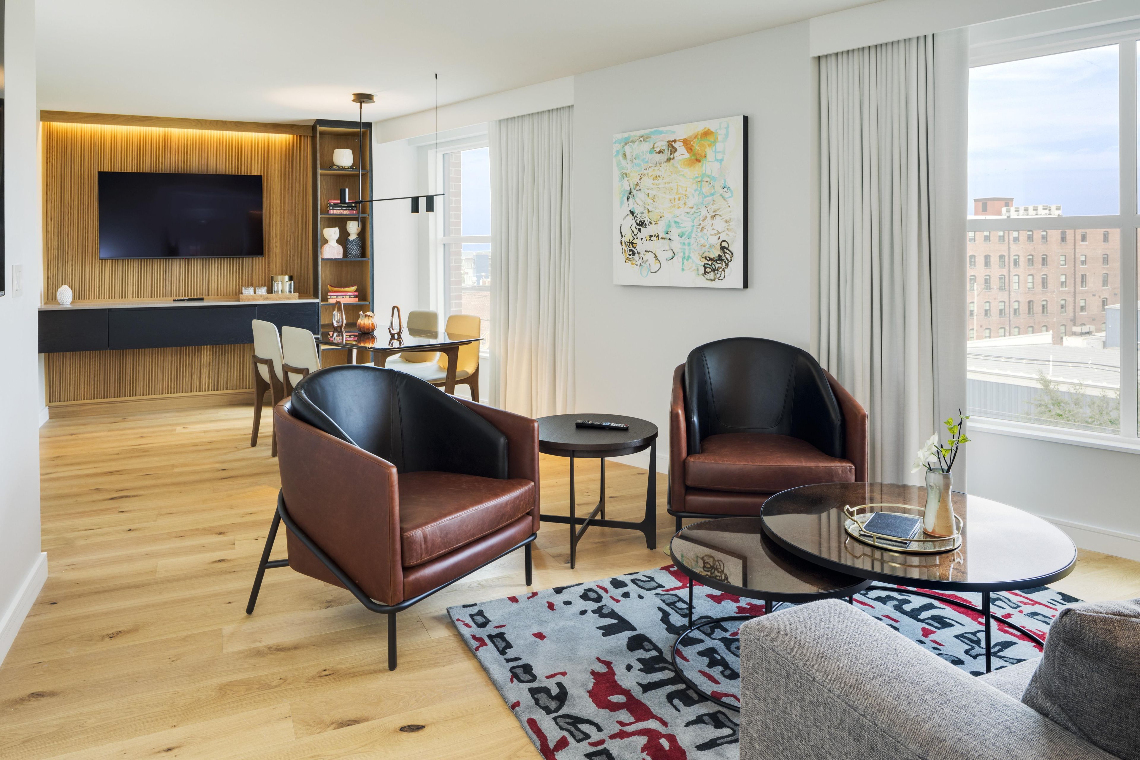 A modern living room with a flat-screen TV, leather armchairs, a coffee table, and a dining area with a glass table and chairs.