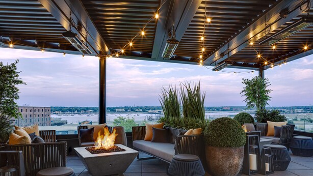 An outdoor seating area with a fire feature, comfortable seating, and a view of the cityscape. - Canopy by Hilton Portland Waterfront (Portland)